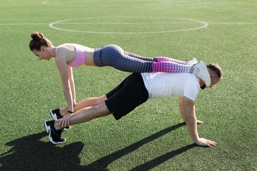 Young guy and a girl train outdoors in the summer, a man does push-UPS and a girl stands on his back and shoulders. Sports lifestyle