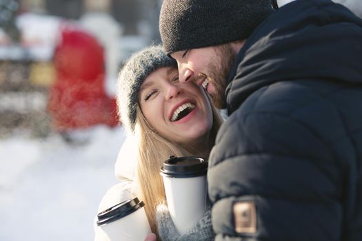 Close-up portrait of a happy couple: men and women hugging and laughing in a winter snow park.