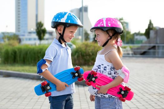 Little brother and sister go skateboarding in the park in the summer, they hit their helmets and smile