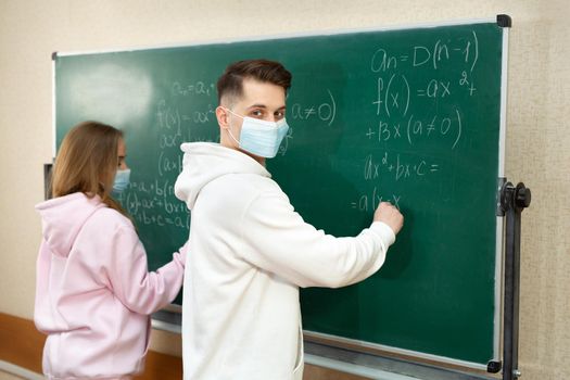 Group of students with face mask writing on the board in the classroom during pandemic