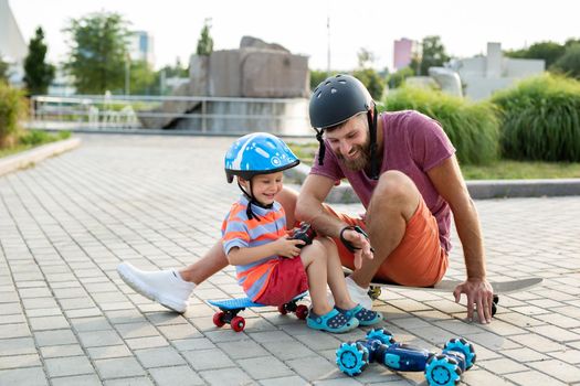 Happy father and son in helmets play in the Park with a robot car that is controlled by a glove while sitting on skateboards.