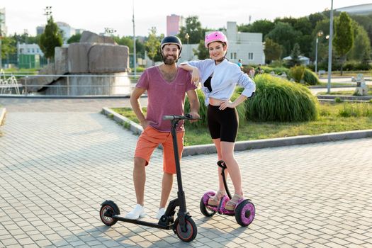 Happy man and woman riding on the hoverboard and scooter in the Park