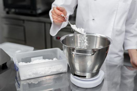 Pastry chef adds powdered sugar to the bowl of the cream mixer.