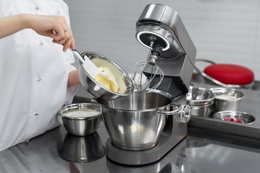Pastry chef adds butter to the kitchen machine, mixer.