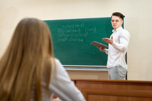 Young student with glasses and a tablet answersat the blackboard.