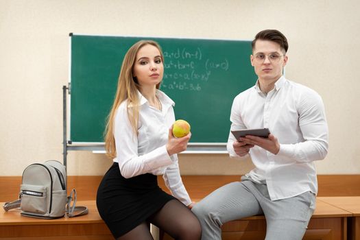 Attractive young students sit on a desk in the classroom on a break.