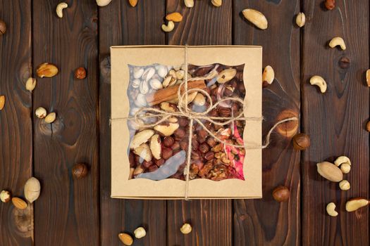Nuts of different varieties in a box on a structural wooden background top view. Assorted nuts in a paper box.