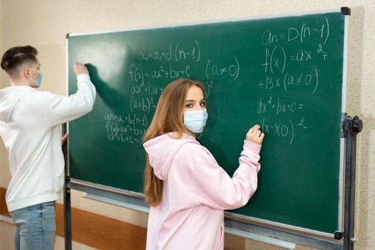 Group of students with face mask writing on the board in the classroom during pandemic