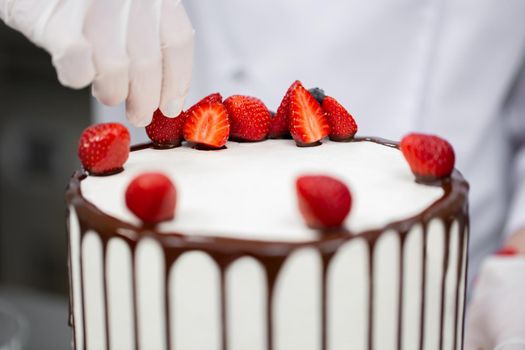 Pastry chef decorates the cake with chocolate streaks of strawberries.