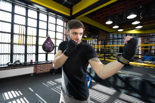 A young athletic male kickboxer clenches his hands into a fist and trains in the ring.