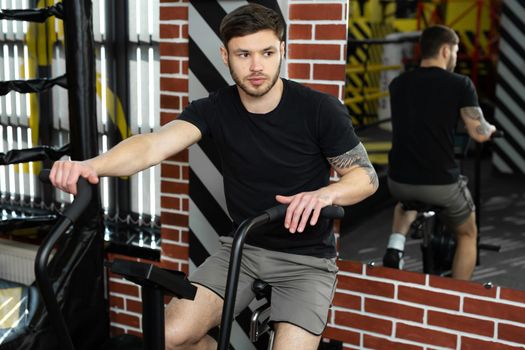 Young athletic male boxer trains on an exercise bike near the ring.