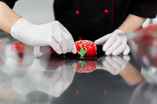 The pastry chef decorates the red mousse cake like a strawberry.