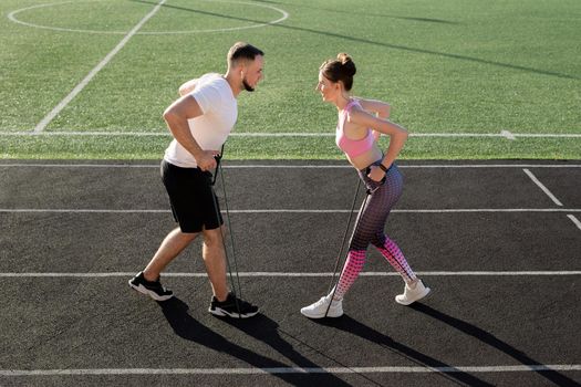 Young fitness couple trains at the stadium in the summer with an elastic expander