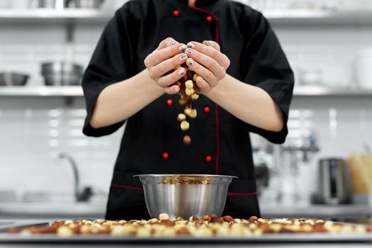 Pastry chef pours a lot of hazelnuts into a bowl for making pralines.
