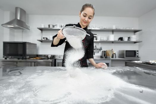 The pastry chef sows the flour through a sieve on the table.