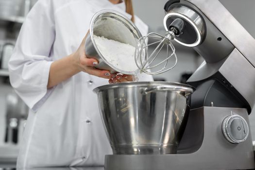 Pastry chef adds flour to the bowl of the mixer.