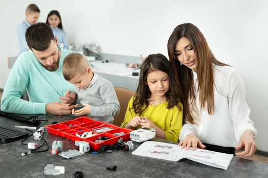 Family with children in a robotics club makes a robot controlled from a constructor.