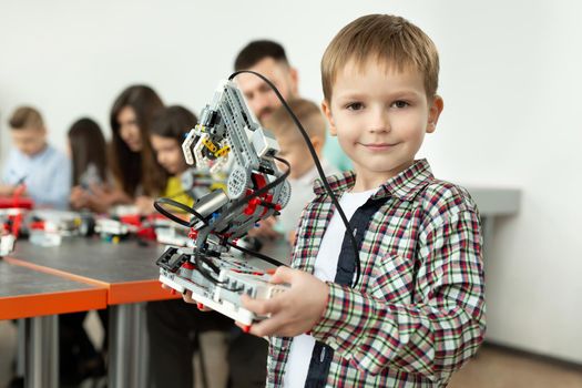 Portrait of a smart boy in a robotics class at school, holding a robot that he assembled from plastic parts programmed on a computer.