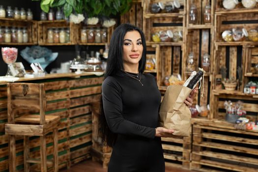 Portrait of a young beautiful woman with a paper bag in her hands in a health food store. Craft bag with bread, sausage and cheese.
