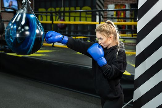 Young female athlete in blue boxing gloves hits a pear in the ring.