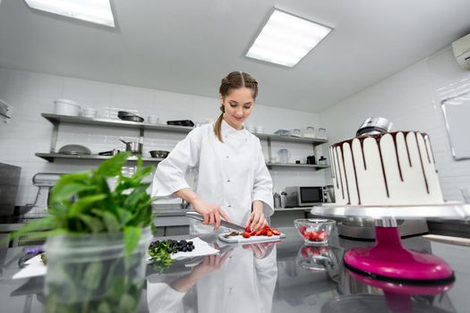 Pastry chef cuts strawberries to decorate the cake