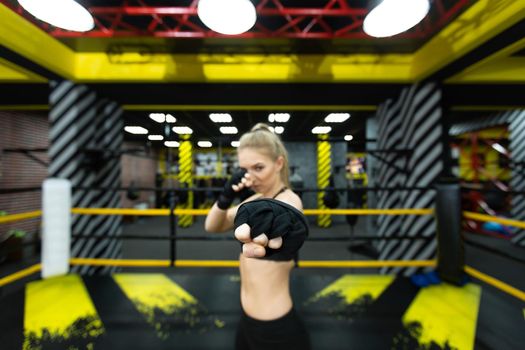 Young sportswoman with boxing bandages looking at camera and punching.