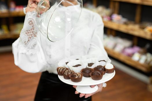 Handmade chocolates on a tray under a glass lid in the hands of a beautiful young woman in the store.