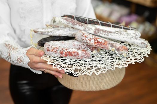 Variety of sausage products close-up on a rustic tray in the hands of a beautiful woman seller.