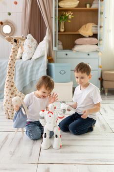 Small children brother and sister sit on the floor in the room, laughing and playing with the robot