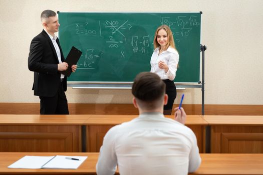 Attractive young female student in a short skirt answers a male teacher near the blackboard.