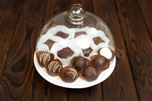 Handmade chocolates on a tray under a glass cover.