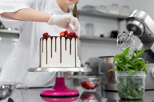 Pastry chef decorates the cake with chocolate streaks of strawberries.