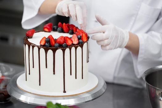 Pastry chef decorates the cake with chocolate streaks of strawberries and blueberries.