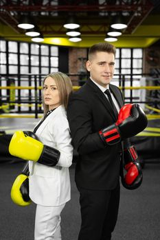 Man and woman in a suit and boxing gloves stand in front of the ring with their backs to each other.