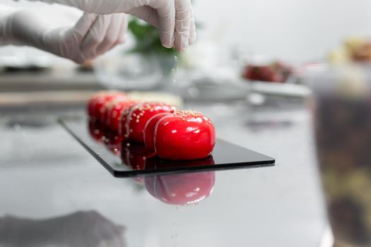 The pastry chef sprinkles the red mousse cake with sesame seeds.