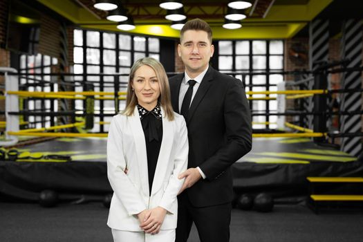 Fellow male and female businessmen in suits pose against the backdrop of a boxing ring.