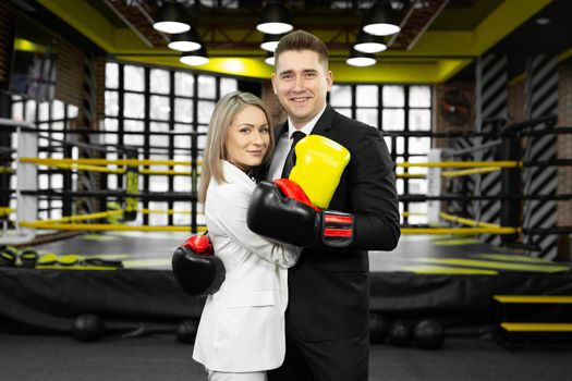 Young married couple, a man and a woman in a suit and boxing gloves embrace in the against of the ring