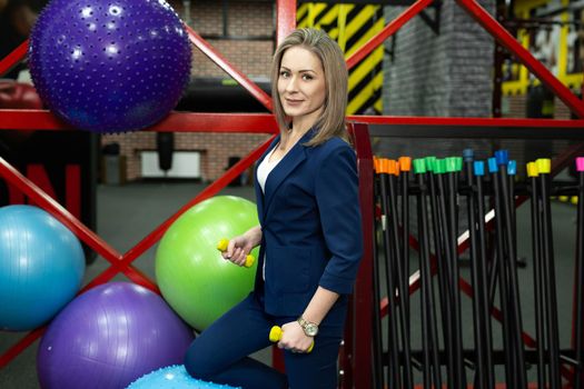 Young beautiful female businesswoman with dumbbells in the gym.