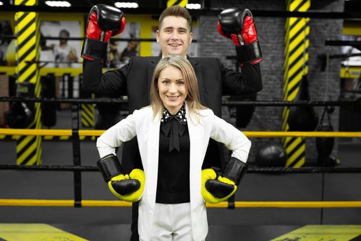 Colleagues, a man and a woman in business suits and boxing gloves in the ring.