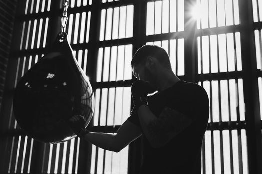 Conceptual portrait of a brutal tattooed boxer who trains in the ring and hits a punching bag. black and white