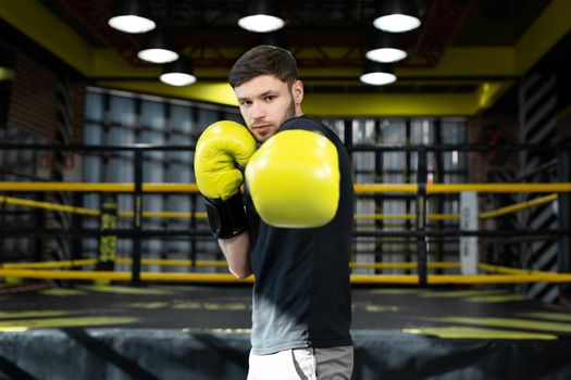 The assembled athlete in the boxing gym practices boxing punches during training and looks at the camera