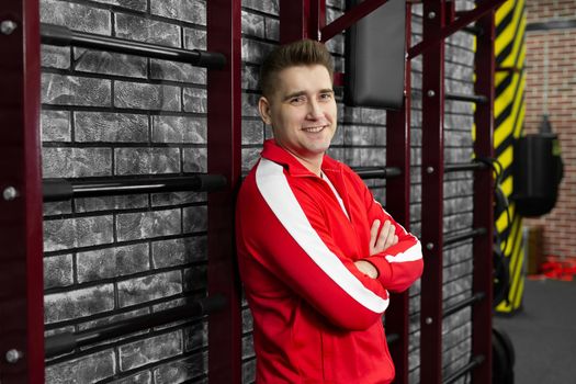 Man in a red tracksuit poses against the wall of the gym.