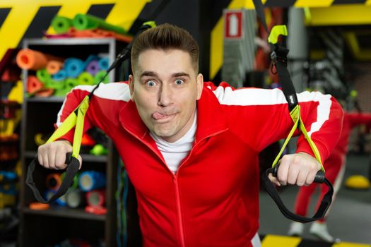 Man in a red tracksuit is working out in the gym, having fun and making faces.