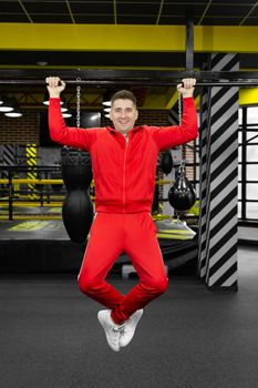 Man in a red tracksuit pulls himself up on a crossbar in the gym.