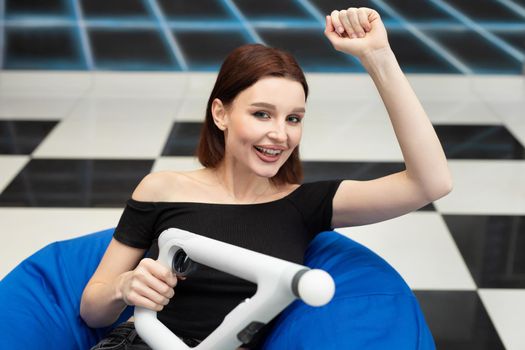 An emotional woman sits in a chair and plays video games console VR with an controller.