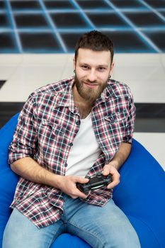 A young happy excited man sits in a chair with a controller in his hands and plays video games and has fun. VR, console gamepad