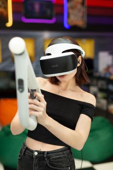Young woman plays on a video games console, an emotional gamer shoots a game using a gun controller in a game club. VR
