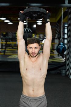 Young muscular guy with a naked torso posing holding a pancake from a barbell