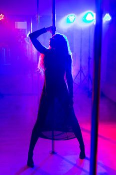 Pole dance. Young slender sexy woman dancing on a pole in the interior of a nightclub with light and smoke.