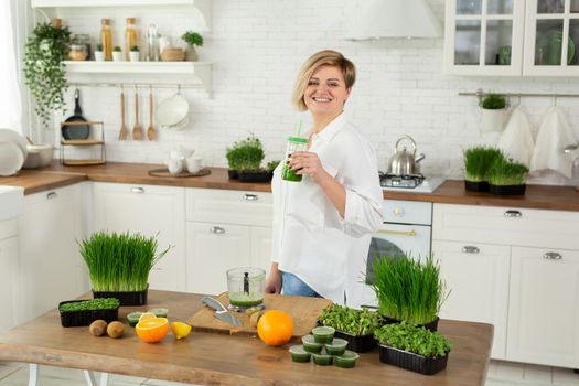 Young beautiful woman drinks a smoothie made from wheat germ juice and micro-greens in the kitchen.